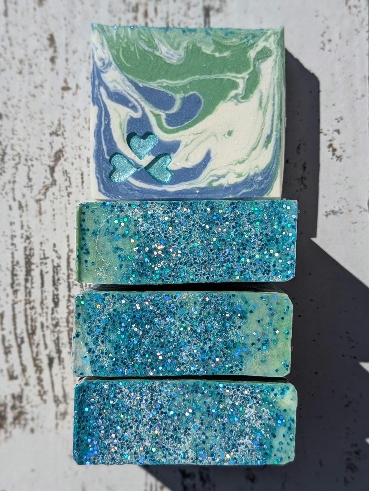 Handmade artisan soap with a stunning swirl of green, blue, and white, accented by shimmering blue heart embeds. The tops sparkle with eco-friendly biodegradable glitter for an extra touch of magic. Crafted with skin-loving ingredients, this luxurious cold-process soap makes a perfect gift or self-care treat!