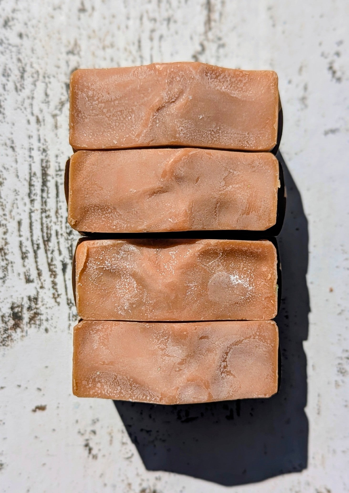 Four rectangular bars of brown soap stacked on a textured white surface