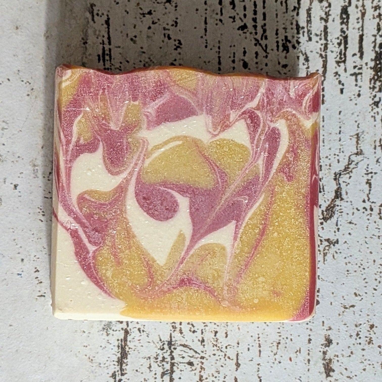 Marbled soap bar with pink and yellow design on a textured white surface