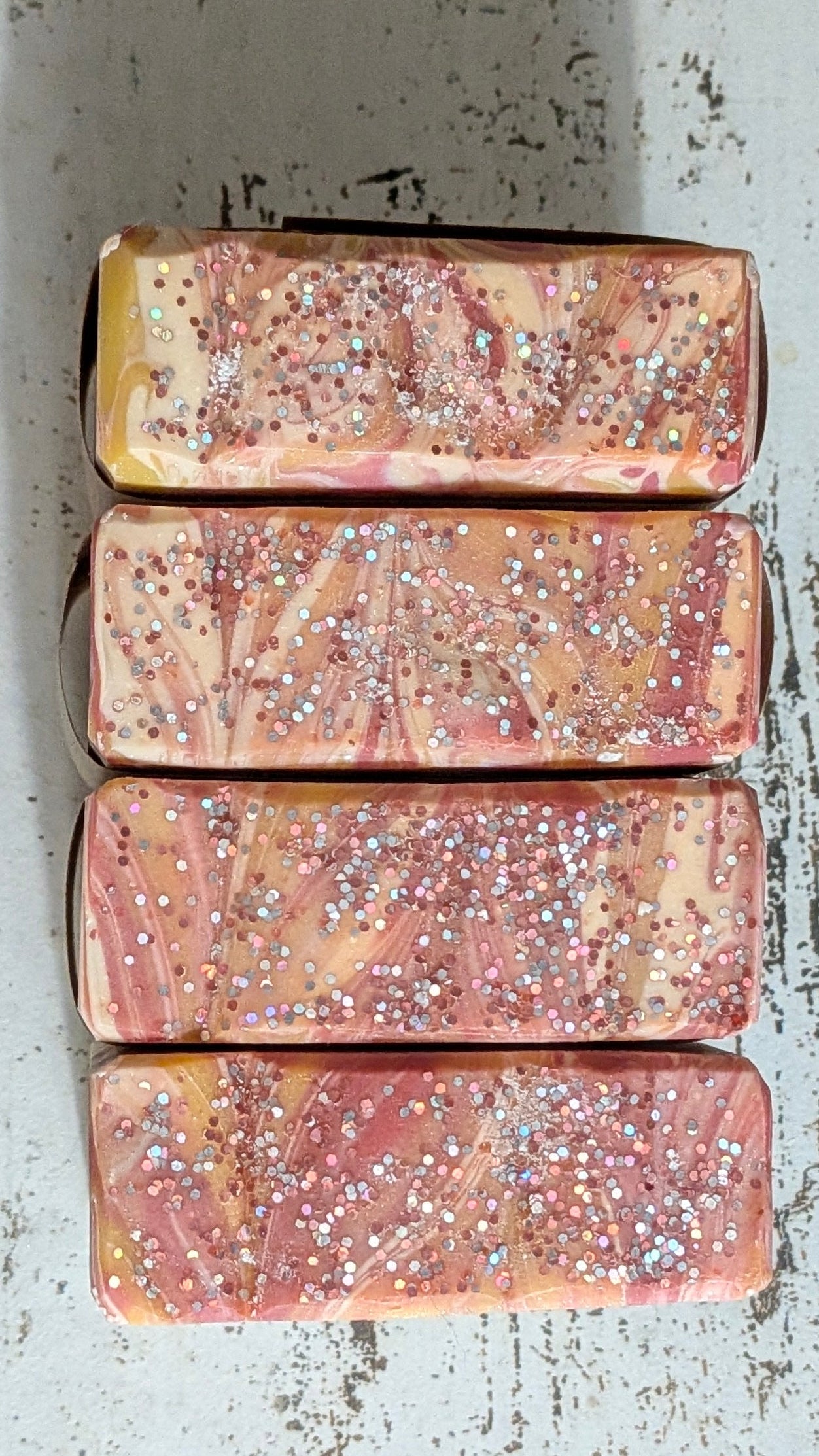 Four rectangular soap bars with glittery texture on a textured surface