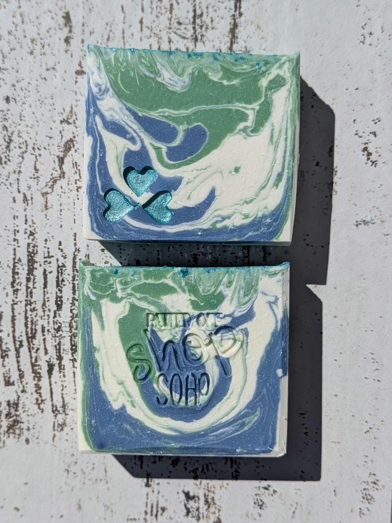Handmade artisan soap with a beautiful swirl of green, blue, and white. One bar features three shimmering blue heart embeds, while the other showcases the &#39;Better Off Soap Shop&#39; stamp. This vibrant, cold-process soap is crafted with skin-loving ingredients and a fresh, clean scent. Perfect for gifting or everyday luxury!