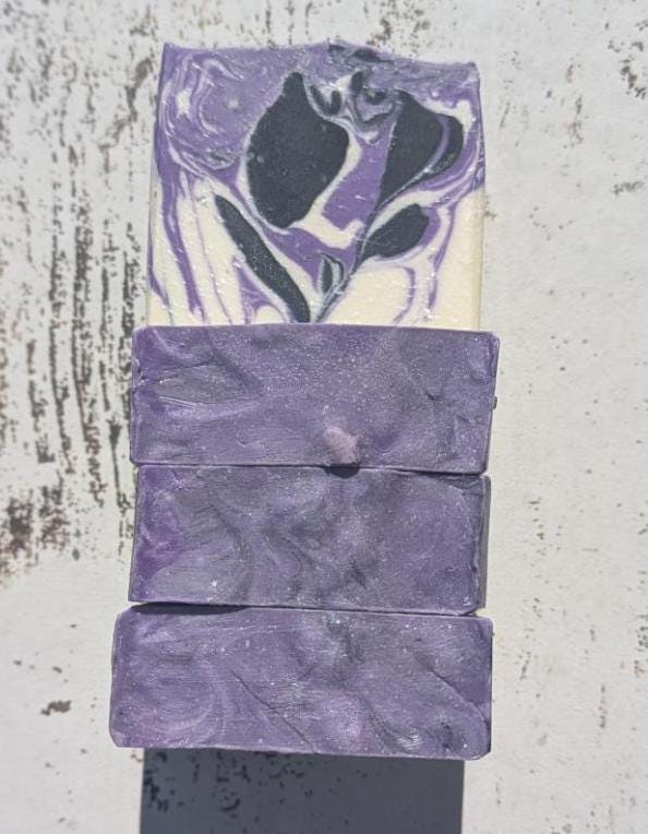 A set of handmade purple, black, and white soap bars standing together, displaying their artistic swirls and bold colors.