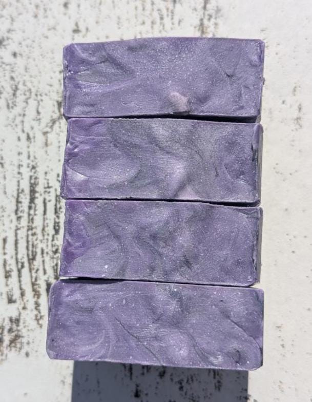 A set of handmade purple, black, and white soap bars standing next to each other together showing off their beautiful textured tops.