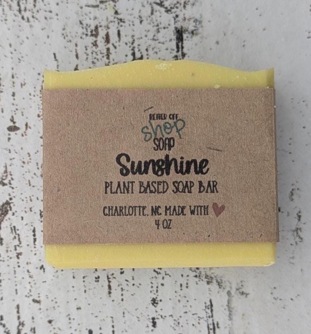 A vibrant yellow handmade cold process soap bar with beveled edges, wrapped in a recyclable paper band. The soap has a fresh, fruity citrus scent with notes of mandarin oranges, bergamot, tangerine, peaches, strawberries, raspberries, and white musk. Made with plant-based ingredients like castor oil, coconut oil, olive oil, and shea butter for a moisturizing lather. Ideal for eco-conscious skincare and daily self-care.