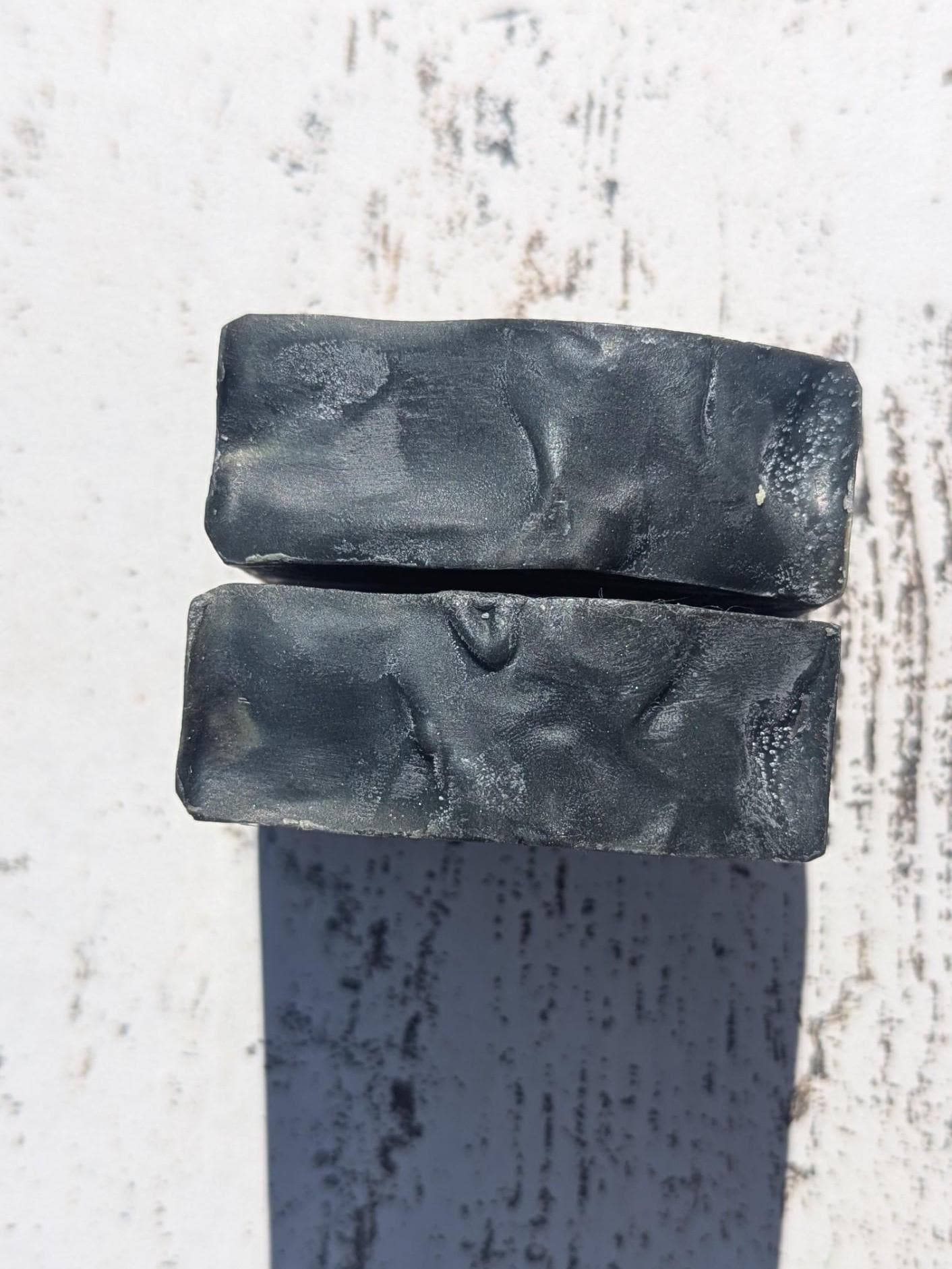 A rustic setting with natural lighting, drawing attention to the soap’s dark gray smooth textured tops, deep mahogany coconut scent inspiration.