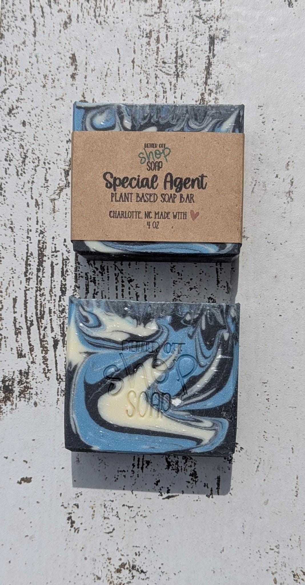 Two Special Agent soap bars stacked vertically on a rustic white wooden surface, with one unwrapped to reveal bold blue, white, and black swirl patterns.