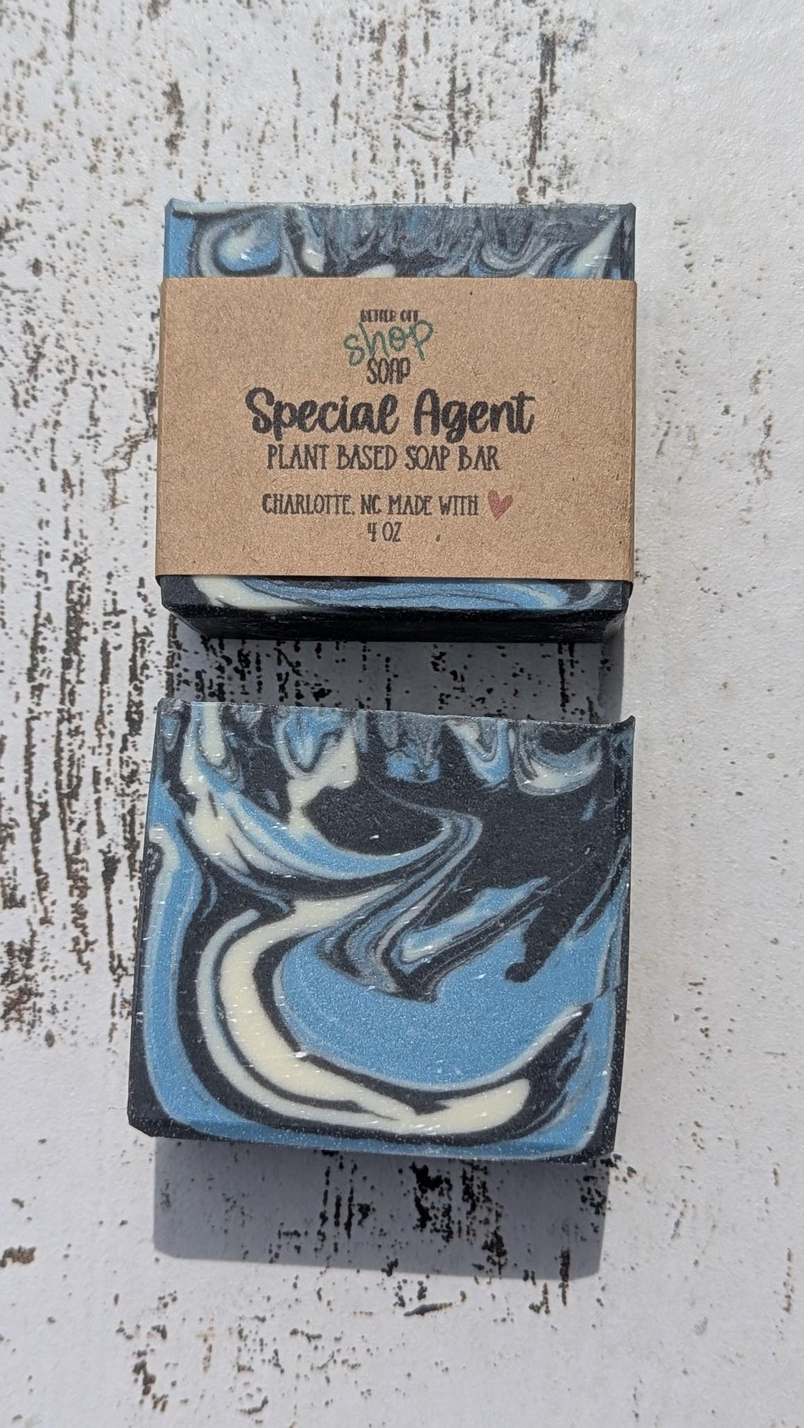 Two Special Agent soap bars stacked vertically on a rustic white wooden surface, with one unwrapped to reveal bold blue, white, and black swirl patterns.