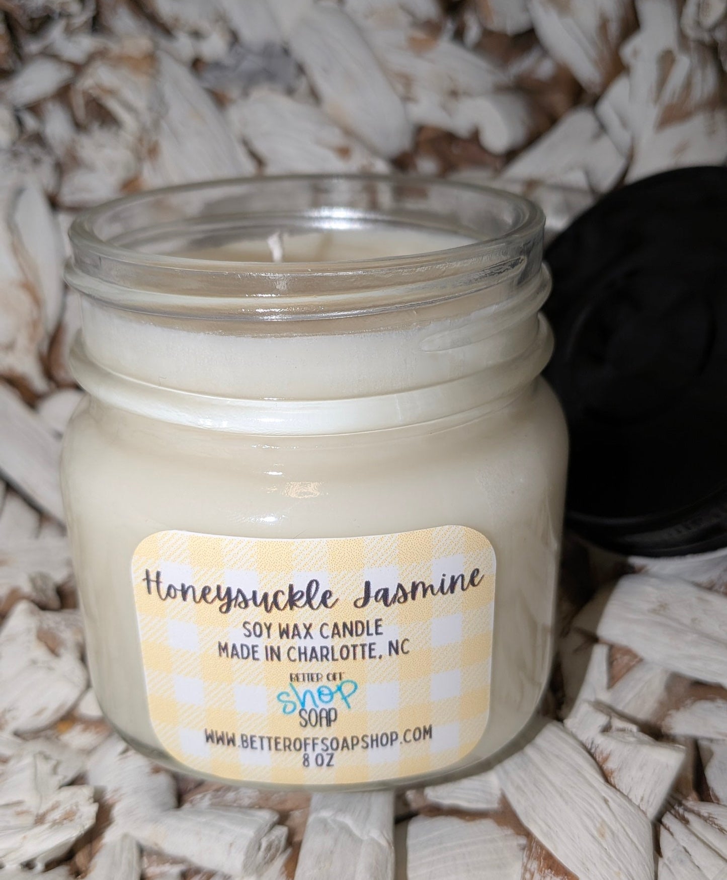 Jar candle labeled 'Honeysuckle Jasmine' on a textured surface