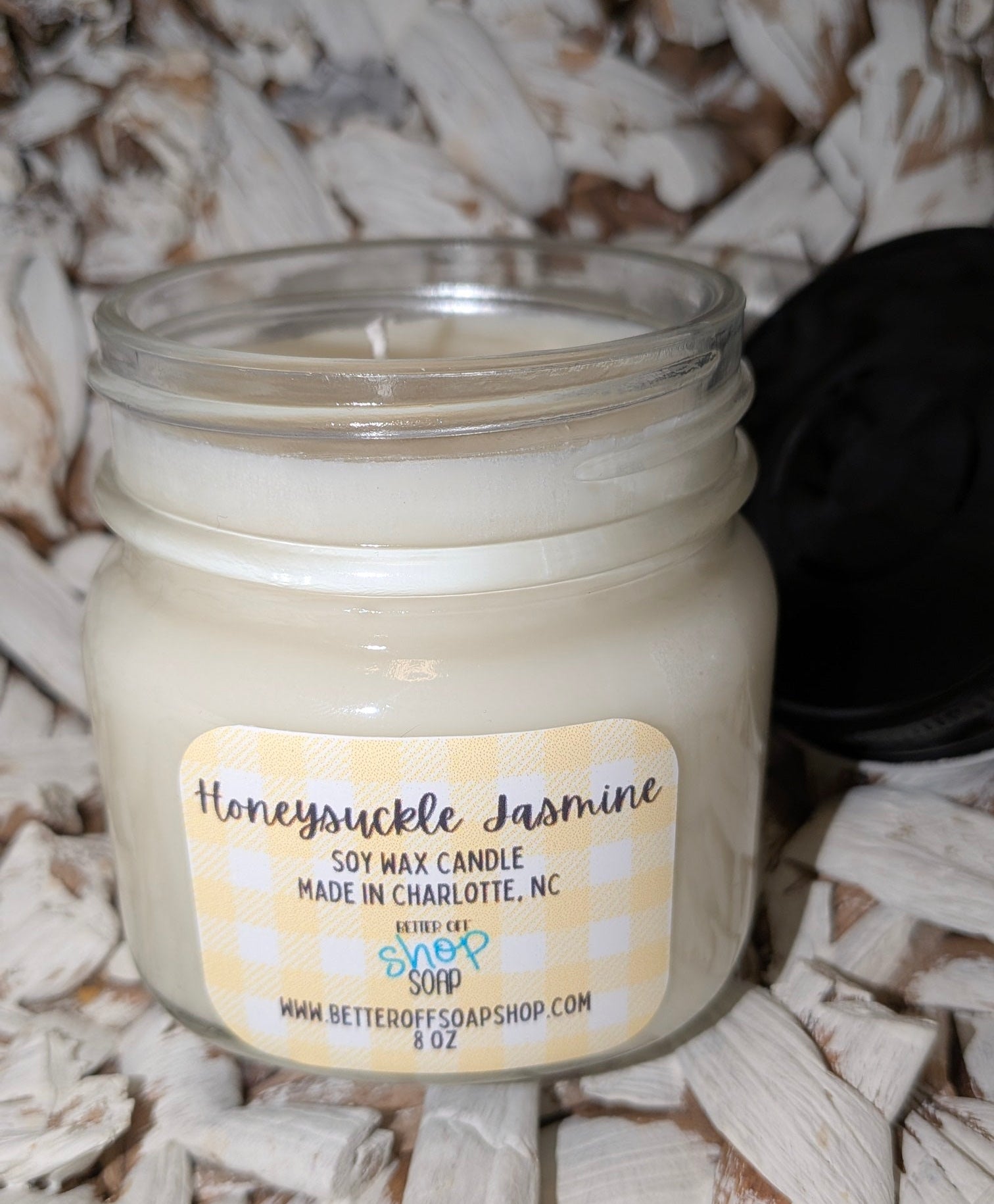 Jar candle labeled 'Honeysuckle Jasmine' on a textured surface