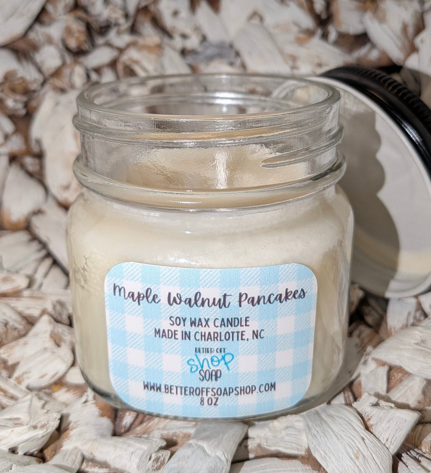 Soy wax candle in a glass jar labeled 'Maple Walnut Pancakes' on a textured surface.