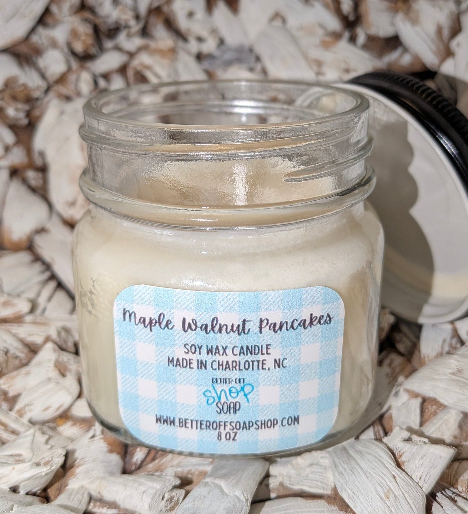 Soy wax candle in a glass jar labeled 'Maple Walnut Pancakes' on a textured surface.