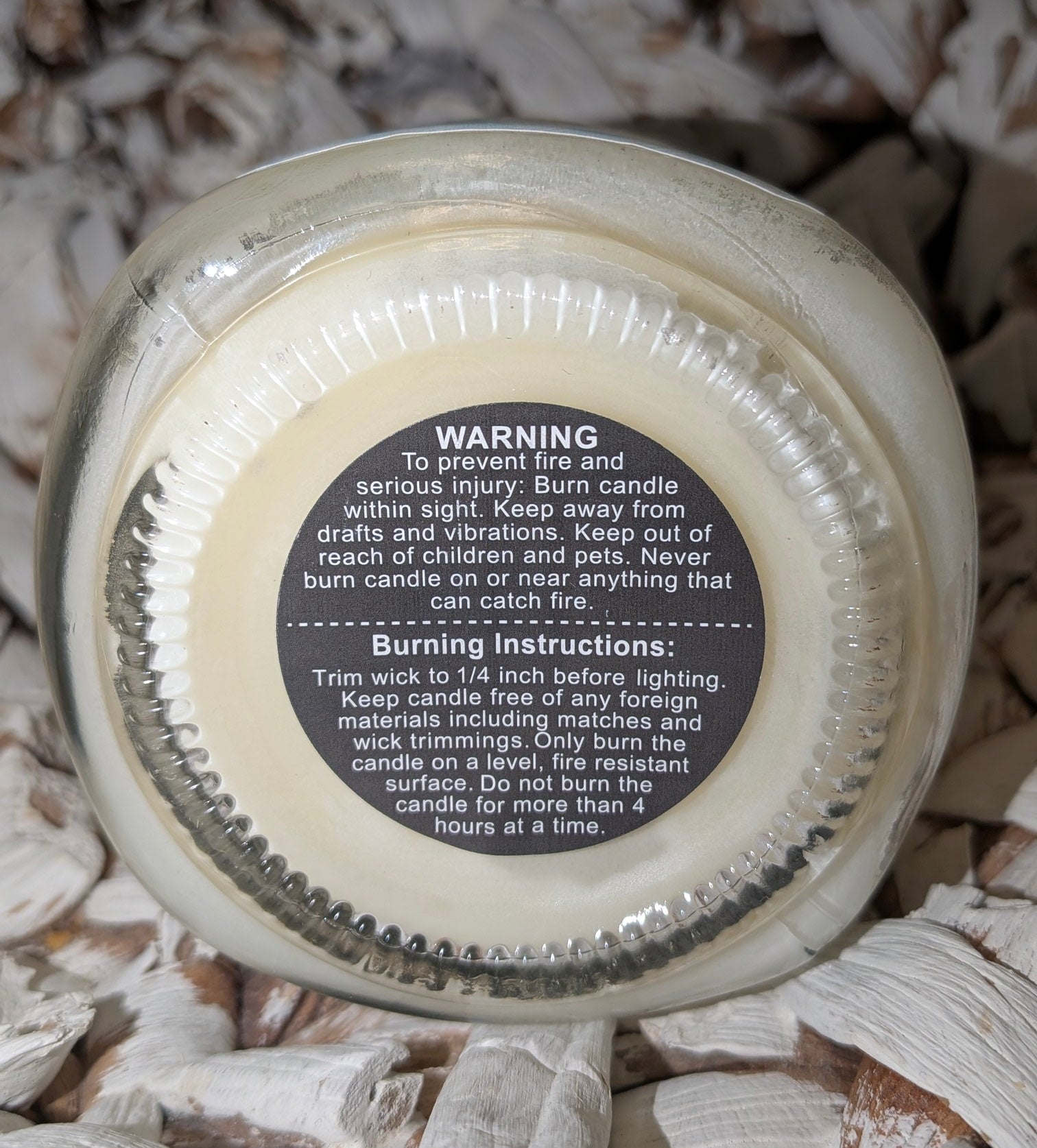 Candle jar lid with warning label on a textured surface