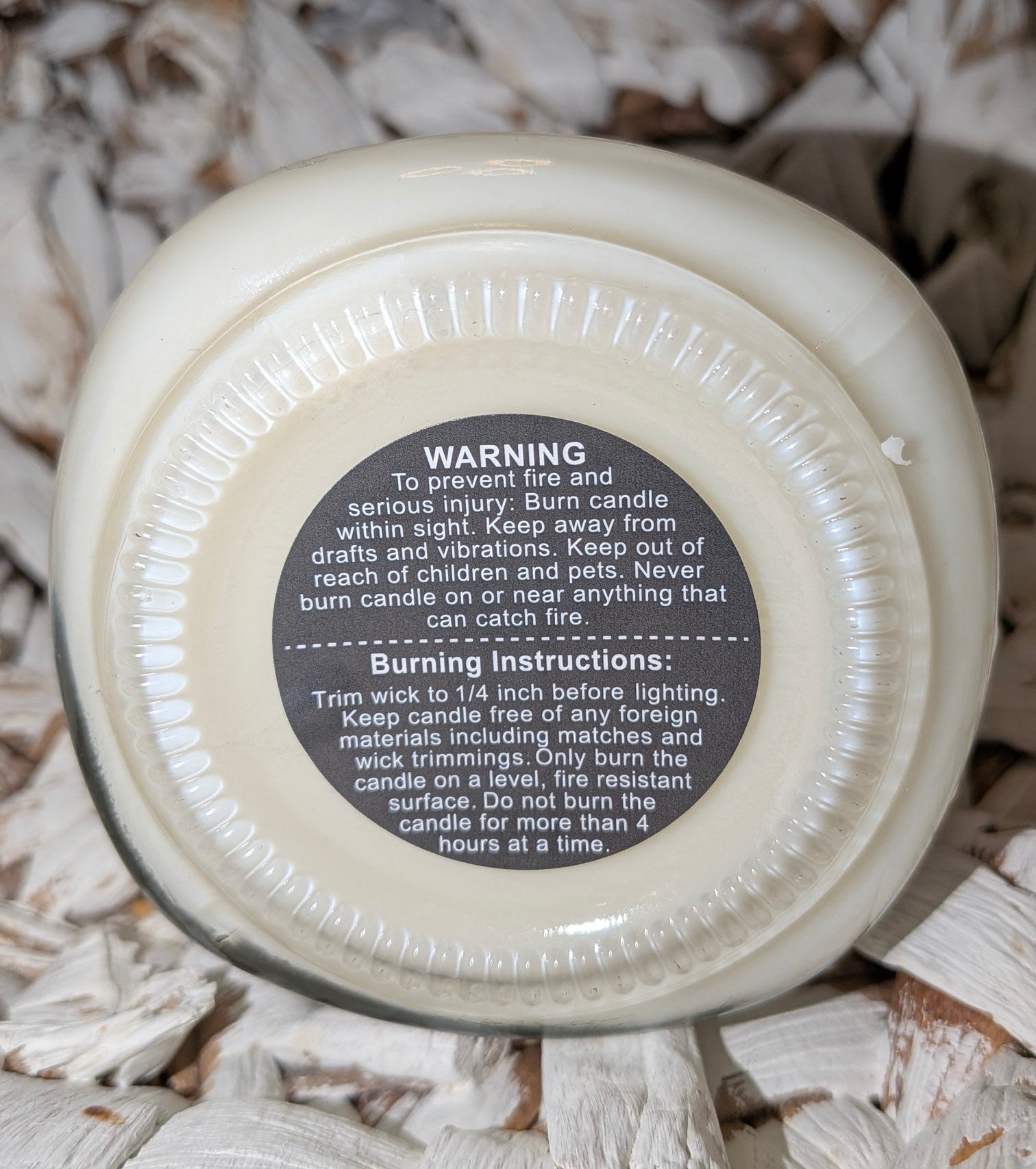 Close-up of a candle lid with warning text on a textured wooden background